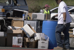 A collection of hazard waste stacked in a rows. A man in a white t-shirt looks over the materials.